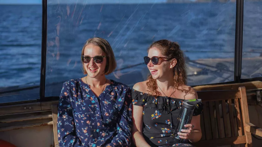 Two women wearing sunglasses sitting on deck and enjoying the sun aboard The Rock Adventure Cruise in the Bay of Islands