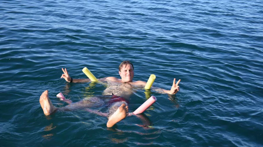 Man floating on the sea with pool noodles and flashing peace signs during The Rock Adventure Cruise in the Bay of Islands
