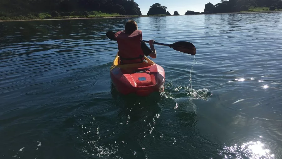 Person kayaking through calm waters near forested islands in the Bay of Islands during The Rock Adventure Cruise