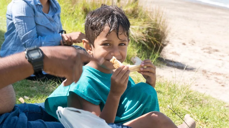 Young boy smiling while eating a sandwich during a beach picnic on The Rock Adventure Cruise in the Bay of Islands