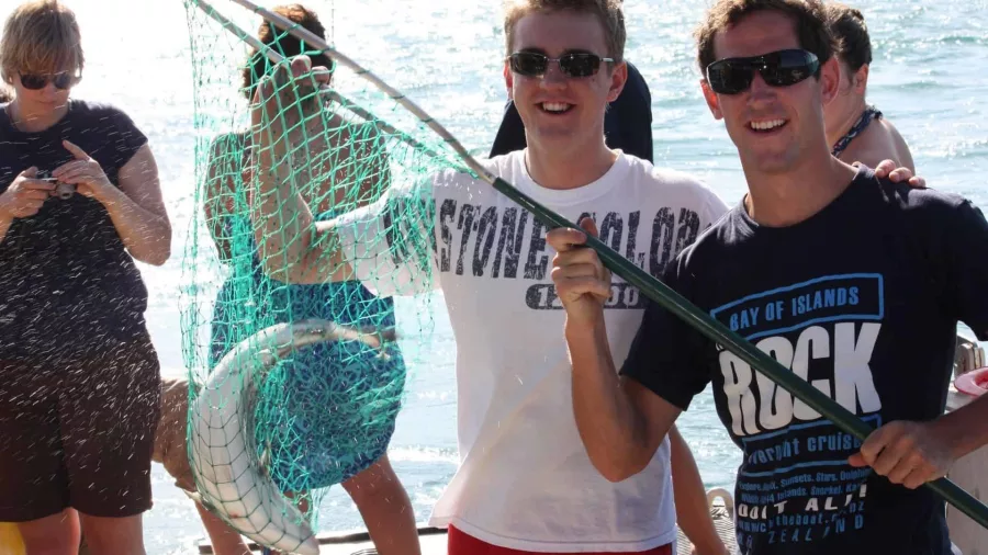Guests holding up a fish in a net on The Rock Adventure Cruise in the Bay of Islands
