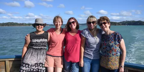 Group of smiling women posing together on the deck of The Rock Adventure Cruise in the Bay of Islands under a sunny sky