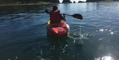 Person kayaking through calm waters near forested islands in the Bay of Islands during The Rock Adventure Cruise