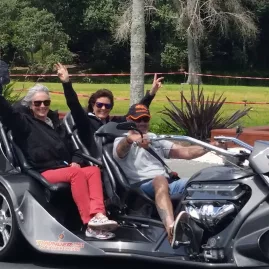 Thunder Trike riders waving while cruising through a scenic town in Northland