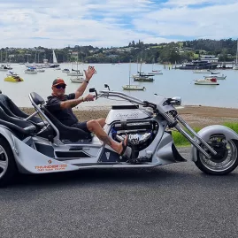 Thunder Trike driver waving while parked along the waterfront in Paihia with boats in the background