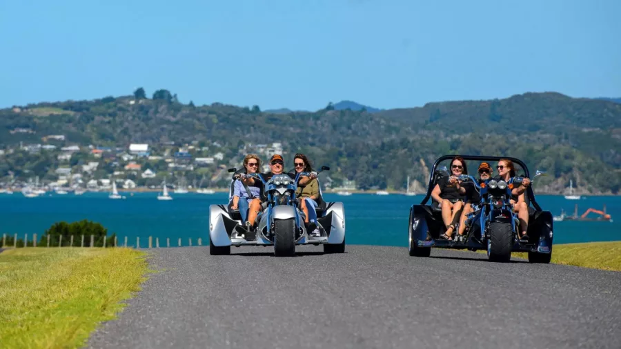 Two Thunder Trike vehicles cruising with passengers along a coastal road in the Bay of Islands