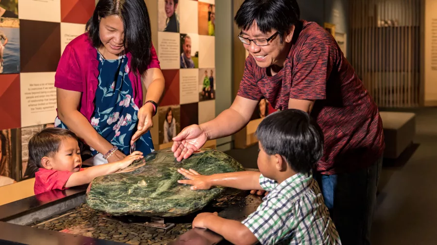 Family touching a large pounamu stone at Te Kōngahu Museum, Waitangi Treaty Grounds, Northland, New Zealand