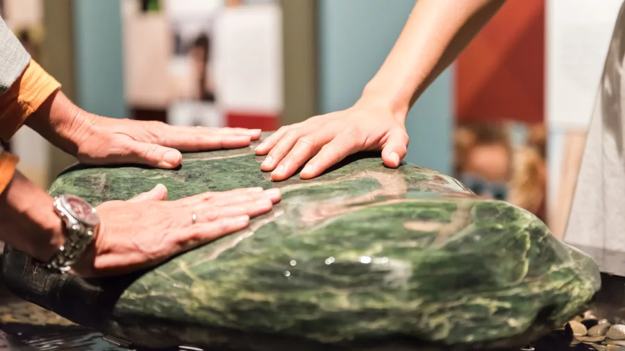Visitors touching a large pounamu stone at Te Kōngahu Museum, Waitangi Treaty Grounds, Northland, New Zealand