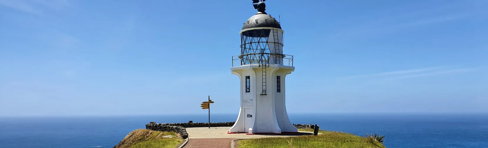 Close-up view of Cape Reinga Lighthouse with directional signpost, Northland, New Zealand