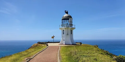 Close-up view of Cape Reinga Lighthouse with directional signpost, Northland, New Zealand