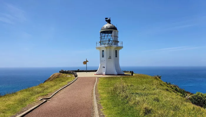 Close-up view of Cape Reinga Lighthouse with directional signpost, Northland, New Zealand