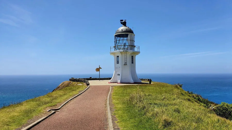 Close-up view of Cape Reinga Lighthouse with directional signpost, Northland, New Zealand