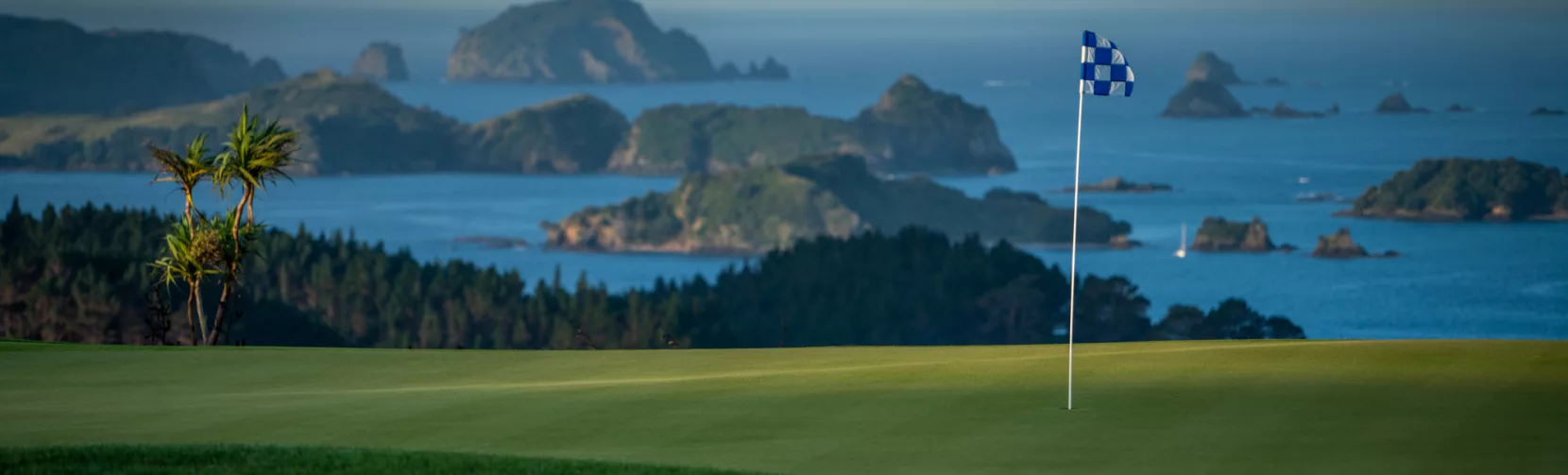 Golf flag on the green at Kauri Cliffs Golf Course with ocean and islands in the background, Bay of Islands, New Zealand