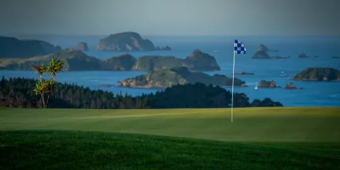 Golf flag on the green at Kauri Cliffs Golf Course with ocean and islands in the background, Bay of Islands, New Zealand