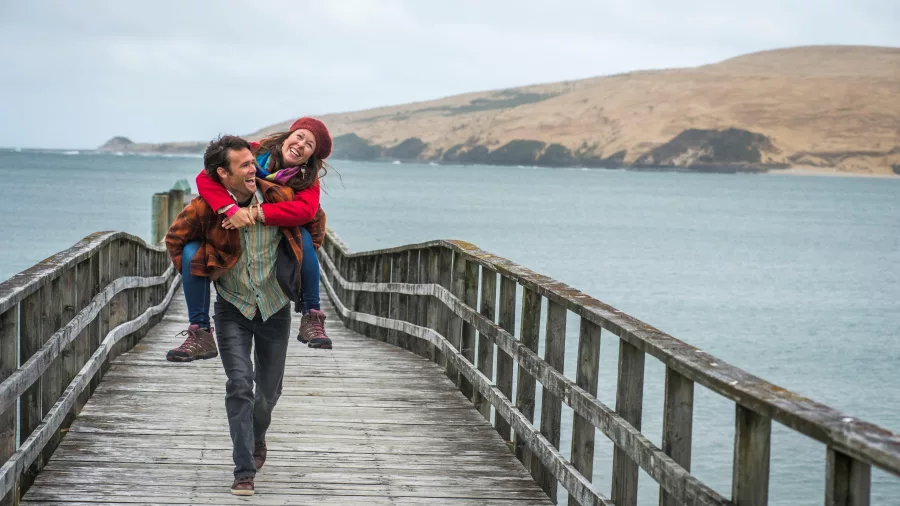 Couple enjoying a playful moment on Ōmāpere Wharf with the Hokianga sand dunes in the background