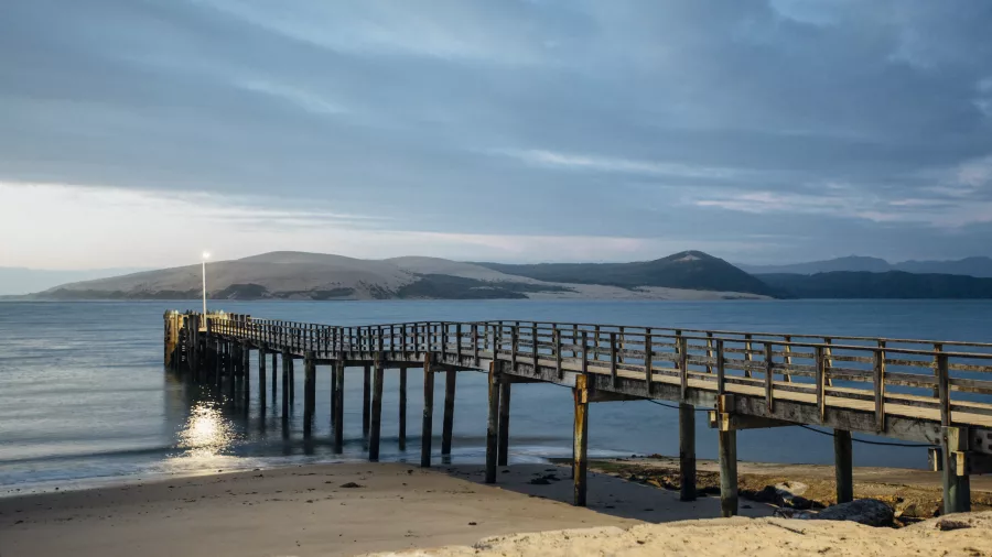 Ōmāpere Wharf at dusk with Hokianga sand dunes in the distance