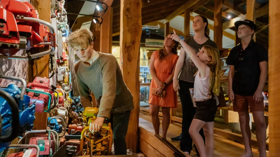 Family looking at a historic chainsaw exhibit with life-sized mannequin at The Kauri Museum
