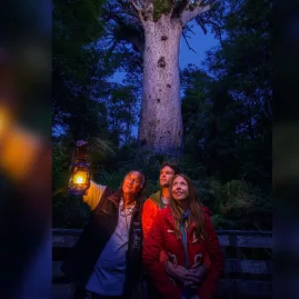 Guests and guide holding a lantern during a night tour in front of Tāne Mahuta in Waipoua Forest