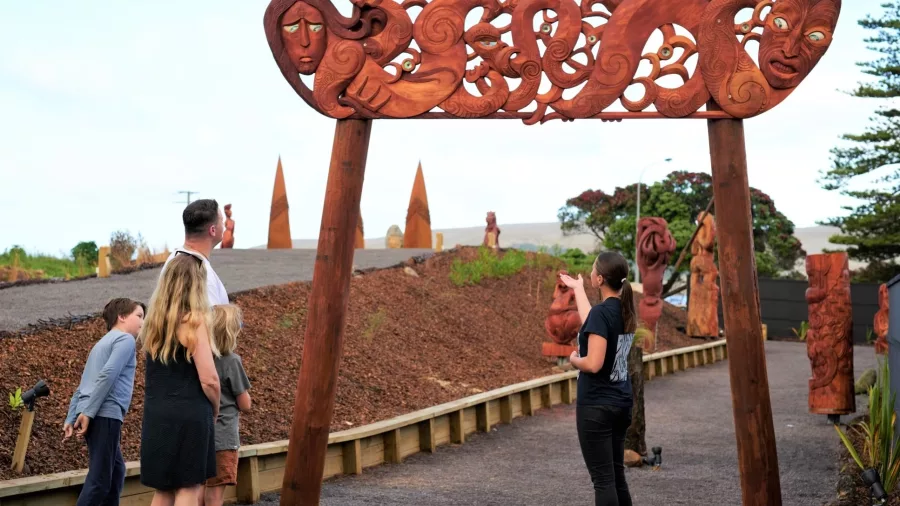Family exploring the intricately carved wooden entrance arch at Manea: Footprints of Kupe, Hokianga