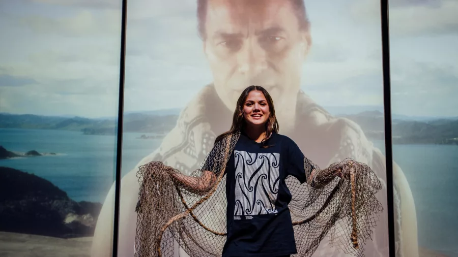 Performer holding a traditional net in front of a large digital projection during a show at Manea 4D Theatre in Northland