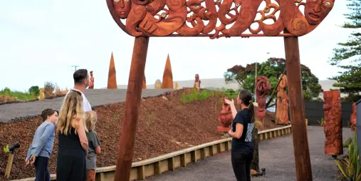 Family exploring the intricately carved wooden entrance arch at Manea: Footprints of Kupe, Hokianga