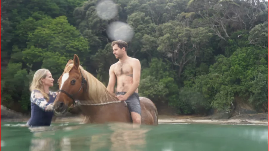 Man on horseback in the water while a woman guides the horse