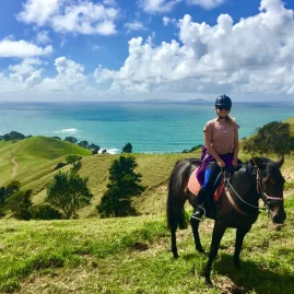 Woman on horseback enjoying panoramic views over green hills and the ocean on the Tuna Trail in Northland