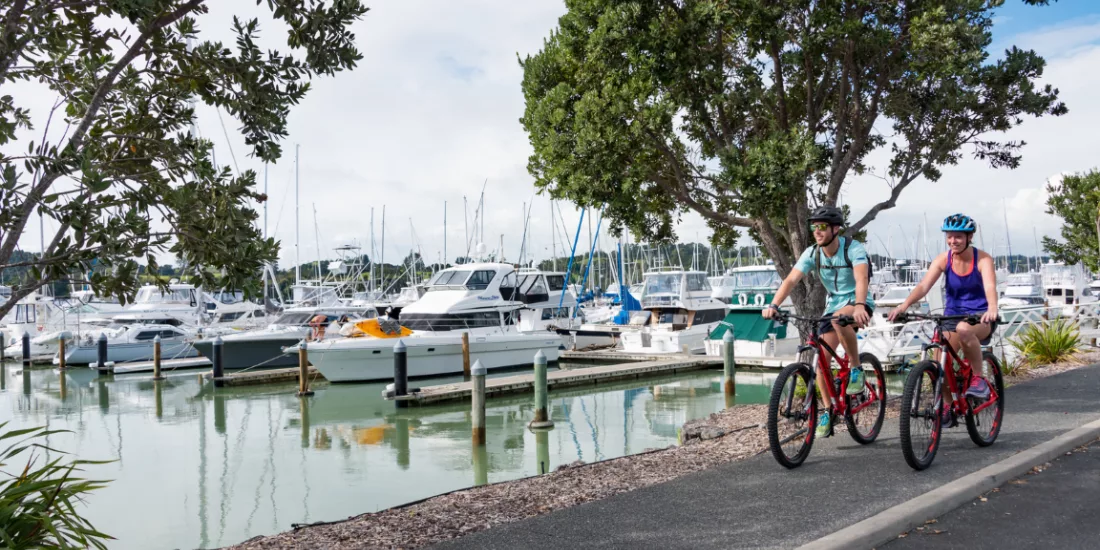 Couple cycling past moored boats along the harbour trail in Ōpua