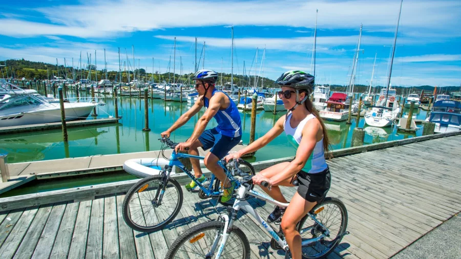Two cyclists riding along the boardwalk at Ōpua Marina on a sunny day