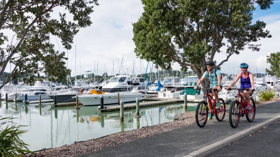 Couple cycling past moored boats along the harbour trail in Ōpua