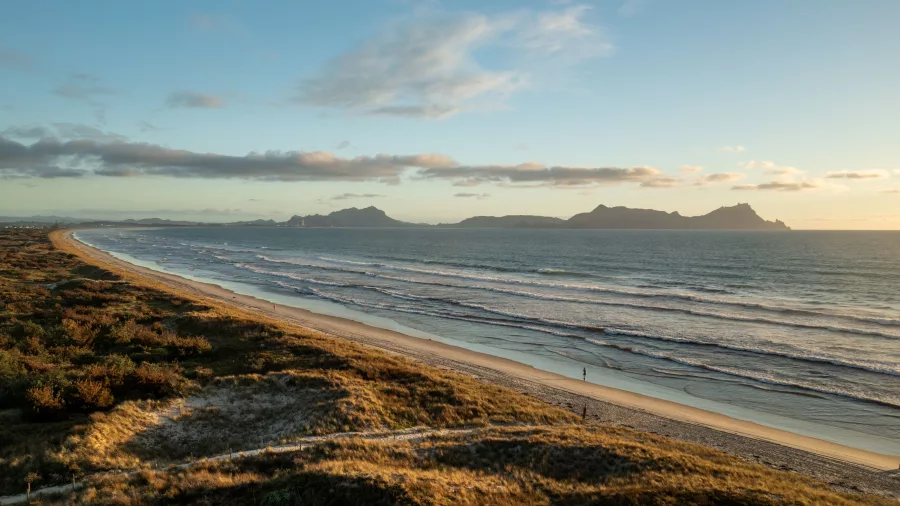 Golden hour light over the long stretch of Bream Bay beach in Northland