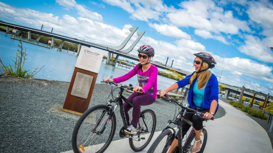 Two women cycling the Hātea Loop shared path by the Whangārei Town Basin with Te Matau a Pohe bridge in the background