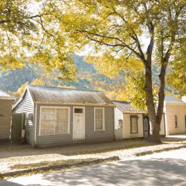 Avenue of historic cottages in Arrowtown surrounded by golden autumn foliage.