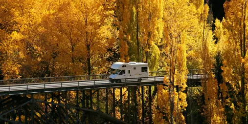 Motorhome crossing Victoria Bridge surrounded by golden autumn trees in Arrowtown, Otago, New Zealand.