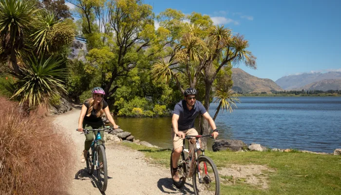 Two cyclists riding along the Lake Hayes trail near Arrowtown in New Zealand on a sunny day.