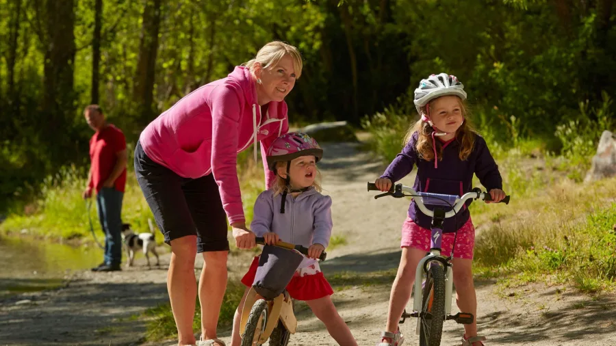 Young family cycling along Arrowtown River Trail in New Zealand on a sunny day.