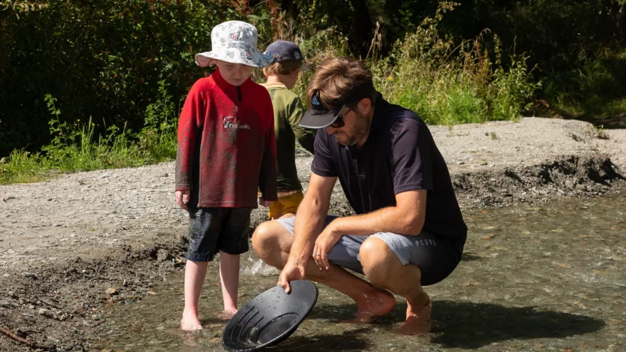 Child watching an adult gold panning in a shallow stream in Arrowtown, New Zealand.