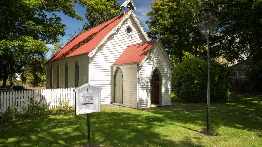 St Paul’s Anglican Church in Arrowtown, New Zealand, a small white wooden church with a red roof surrounded by trees and a white picket fence.