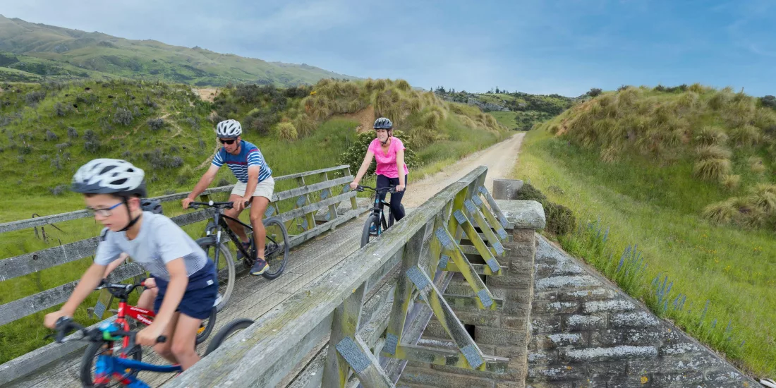 Family riding bikes across wooden bridge near Middlemarch on the Otago Central Rail Trail