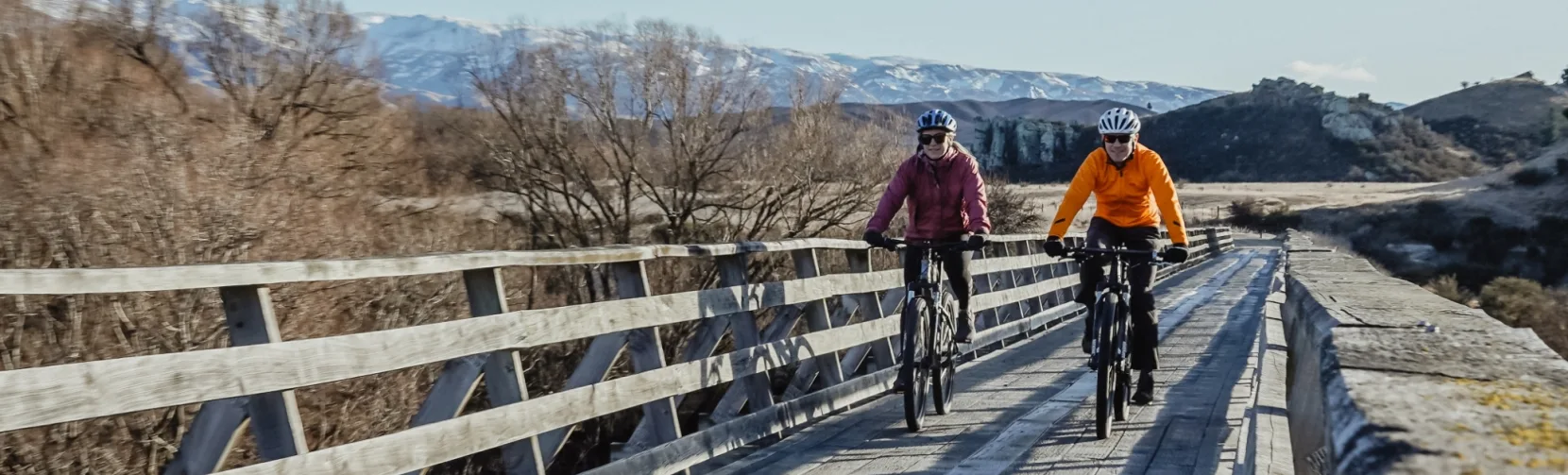 Cyclists riding over bridge in winter scenery along Otago Central Rail Trail