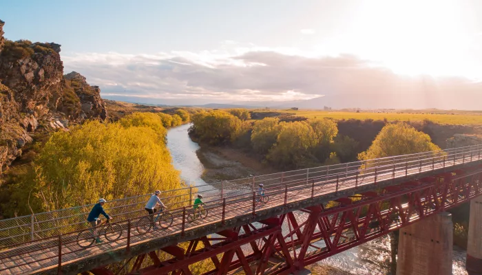 Family cycling across rail trail bridge at sunrise in Central Otago