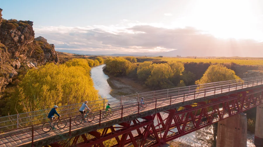 Family cycling across rail trail bridge at sunrise in Central Otago