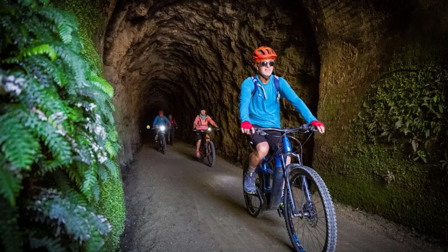 Group of cyclists riding through a rocky tunnel on the Clutha Gold Cycle Trail in Central Otago, New Zealand