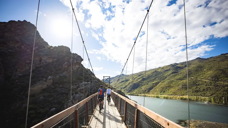 Cyclists crossing a suspension bridge high above Lake Dunstan on the trail from Cromwell to Clyde.