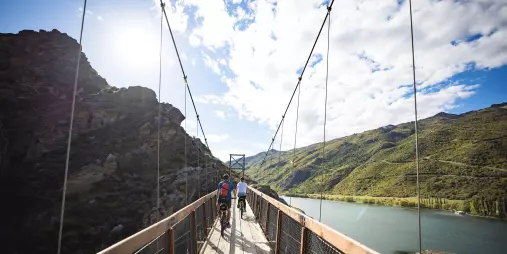 Cyclists crossing a suspension bridge high above Lake Dunstan on the trail from Cromwell to Clyde.