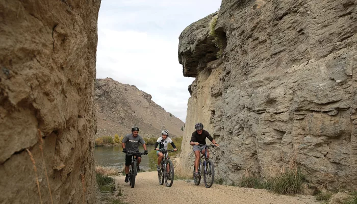 Three cyclists riding through the rocky landscape of the Roxburgh Gorge Cycle Trail near Alexandra in Central Otago, New Zealand