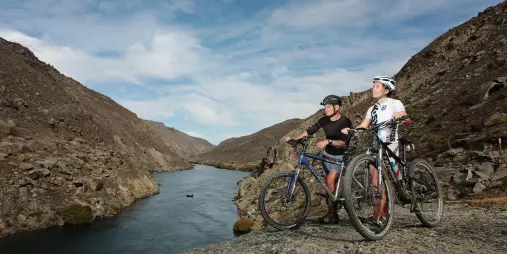 Two cyclists pause to enjoy the Clutha River views along the Roxburgh Gorge Cycle Trail near Alexandra in Central Otago, New Zealand