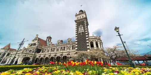 Dunedin Railway Station in spring, with colourful tulips and flowers blooming in the foreground.
