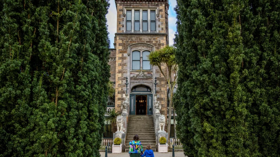 Family approaching the entrance of Larnach Castle, framed by tall hedging.
