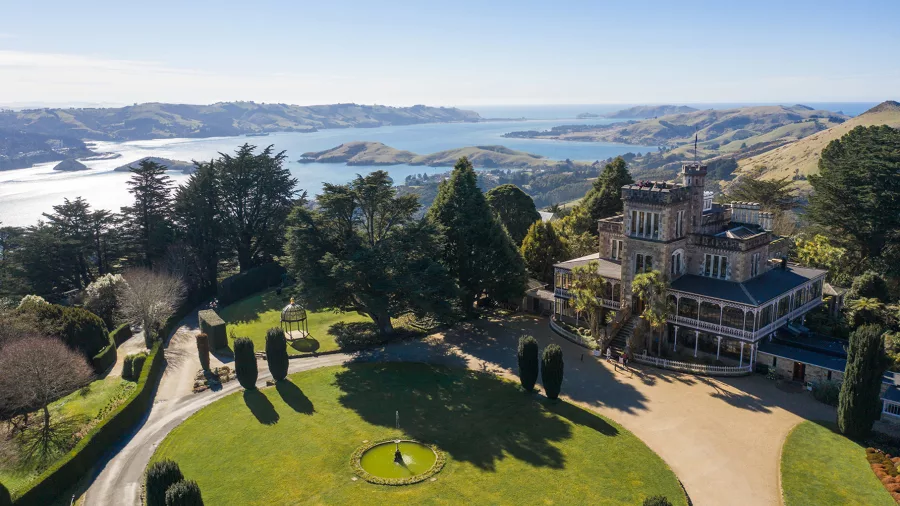 Aerial view of Larnach Castle with Otago Peninsula coastline in the distance.